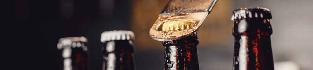 Glass ice cold bottles of beer with opener cap on dark background.