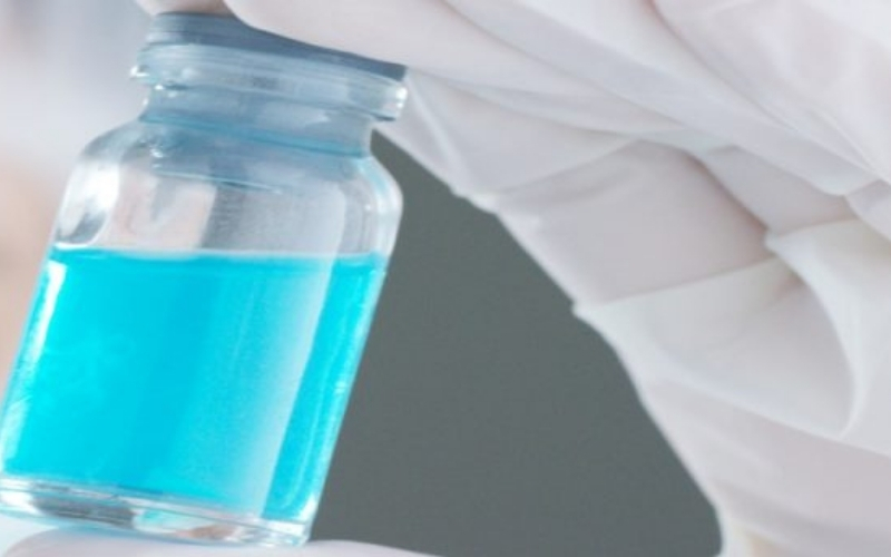 scientist looking at a blue vial held in their hand