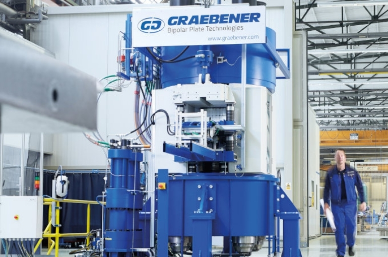 Graebener® Bipolar Plate Technologies Bipolar Plate machinery in a factory setting with a man in blue walking next to it