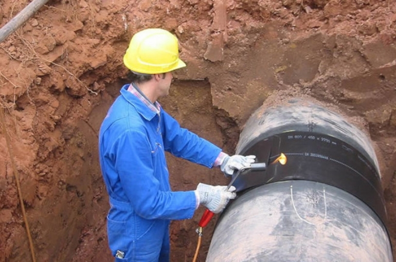 Dipl.-Ing. Dr. E. Vogelsang GmbH & Co. KG 's corrosion protection materials for pipes, pipelines and flanges with a man in blue and a yellow hardhat working on a pipeline underground